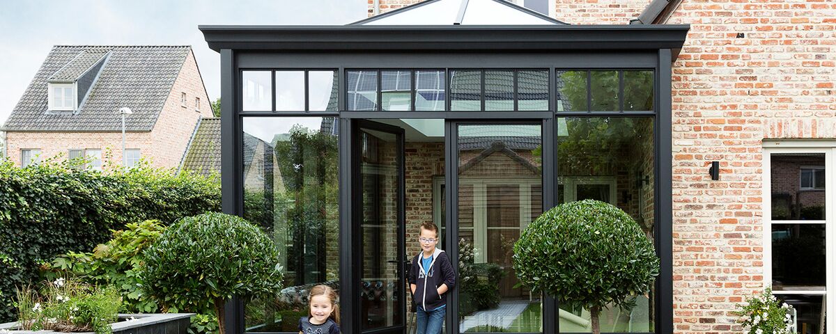 Children playing in the garden in front of black Reynaers Aluminium conservatory.